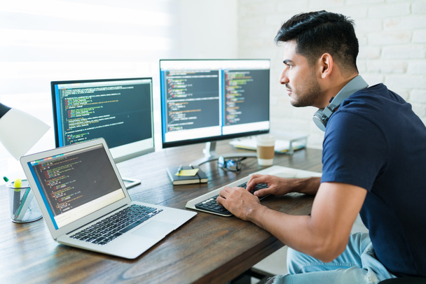 Vista lateral de la atractiva programación de desarrolladores de software hispanos usando computadora mientras trabajan desde casa
 - Foto, imagen