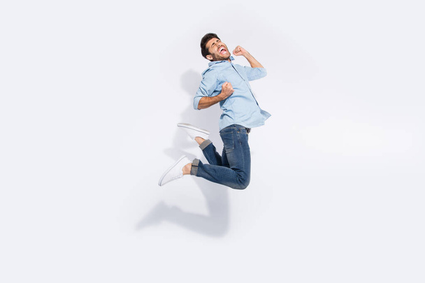 Full body profile photo of multiethnic guy jumping high rejoicing of great win raising arms screaming wear casual denim outfit isolated white color background - Photo, image