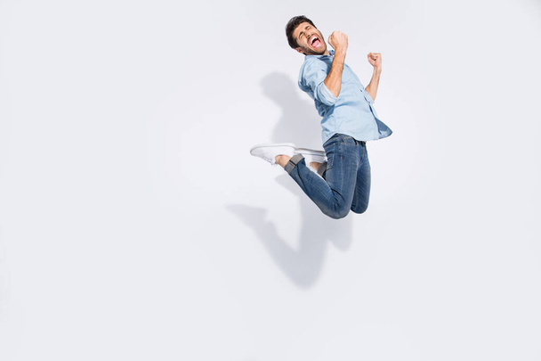Full body profile photo of funny arabian guy jumping high rejoicing of great win raising fists wear casual denim shirt isolated white color background - 写真・画像