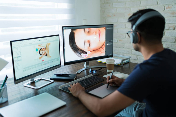 männlicher Fotograf trägt Kopfhörer beim Bearbeiten von Fotos mit Grafik-Tablet am Schreibtisch - Foto, Bild