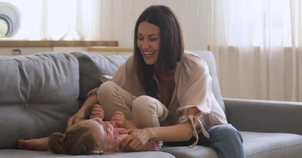 Happy young mom playing with cute kid daughter on sofa - Záběry, video