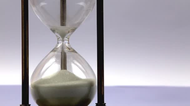 Closeup of a sand clock on the left side with space on the right side. Closeup of a glass sand clock on white with golden balls instead of sand falling. Time - Footage, Video