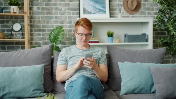 Slow motion of happy teenage boy enjoying social media using smartphone at home - Кадры, видео