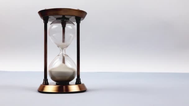 Closeup of a sand clock in the middle of the frame space on the right side. Closeup of a glass sand clock on white with golden balls instead of sand falling measuring time. Deadline - Footage, Video