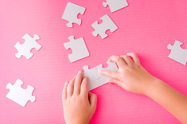 children's hands fold a paper white puzzle on a pink background development of fine motor skills of hands - Foto, Bild