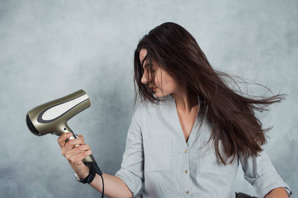A young woman with long dark hair uses a hair dryer to dry and style. Hairstyle styling and hair care, - Foto, imagen