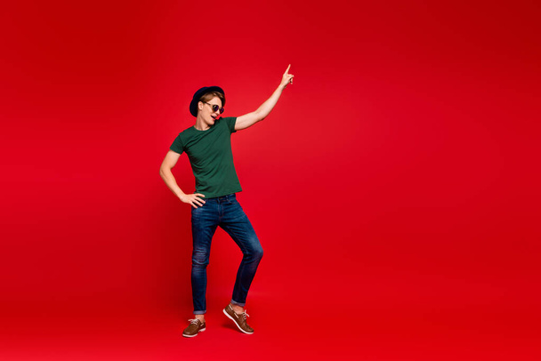 Full size profile side photo of crazy guy have fun on summer weekends celebration aprty dance raise index finger wear denim jeans sneakers outfit isolated over red color background - Foto, Bild