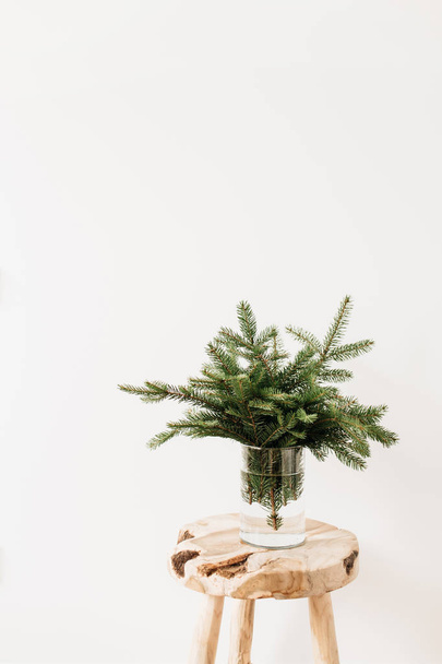 白い背景にしっかりとした木製のスツールにモミの枝で作られた花束。最小限のクリスマス構成. - 写真・画像