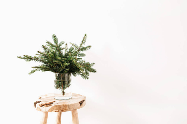Ramillete de ramas de abeto sobre taburete de madera maciza sobre fondo blanco. Composición minimalista de Navidad
. - Foto, Imagen