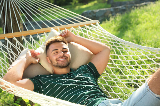 Young man resting in comfortable hammock at green garden - Фото, изображение