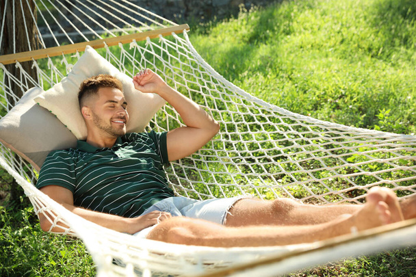 Young man resting in comfortable hammock at green garden - Fotografie, Obrázek