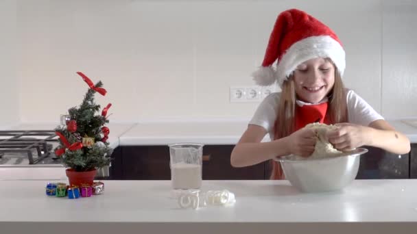 Cute girl nastolatek w kapeluszu Świętego Mikołaja i czerwony fartuch świąteczny tnie ciasteczka z ciasta własnymi rękami. Szczęśliwego Nowego Roku i Bożego Narodzenia - Materiał filmowy, wideo
