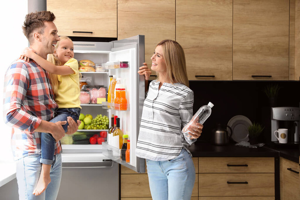 Happy family with bottle of water near refrigerator in kitchen - Foto, afbeelding