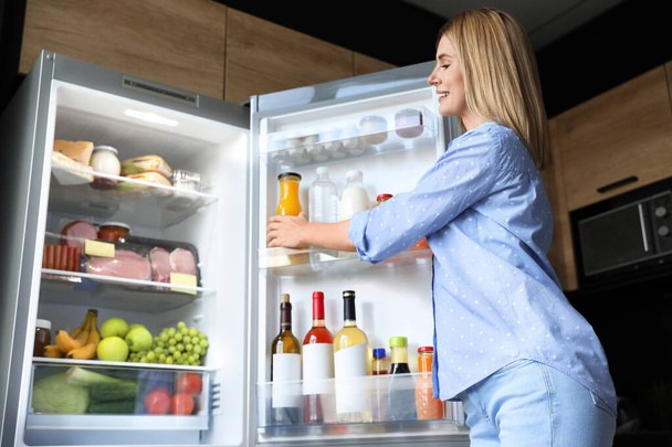 Woman taking bottle with juice out of refrigerator in kitchen - Photo, Image
