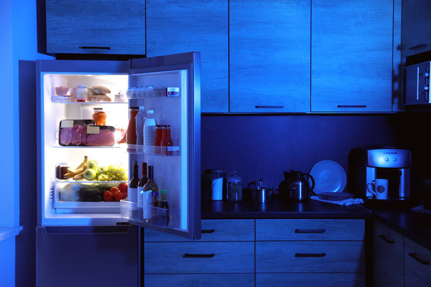 Открытый холодильник, полный продуктов на кухне ночью
 - Фото, изображение