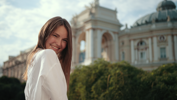 fiatal lány fehér blúzban, pózol mosollyal a kamera előtt az utcán - Felvétel, videó