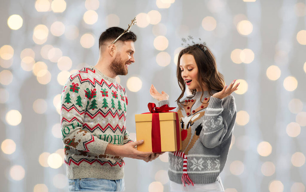 happy couple in ugly sweaters with christmas gift - Fotó, kép