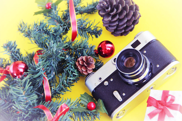 film vintage fotocamera met een tak van een groene boom en kerstdecor op een gele achtergrond - Foto, afbeelding