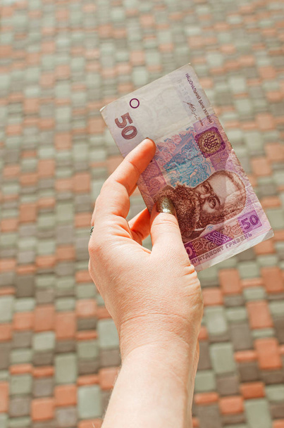 female hand holds a 50 hryvnia bill against a street background. - Photo, Image
