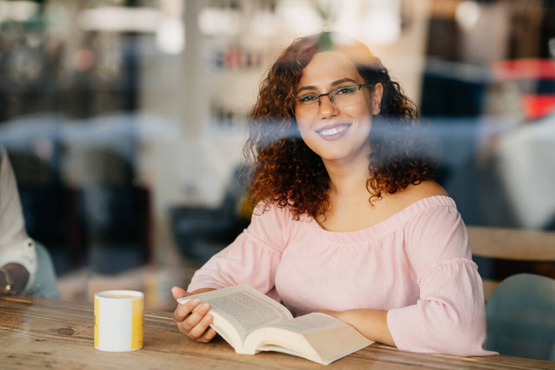 Young woman with eyeglasses reading book in cafe - Photo, image