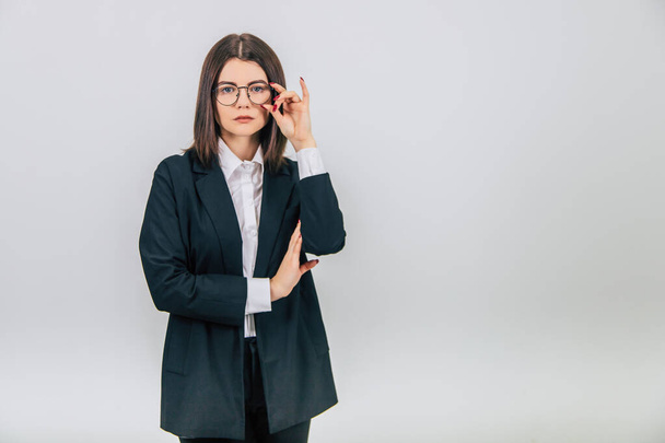 Attractive serious businesswoman in black suit standing, readjusting her glasses, looking at the camera. - Фото, зображення