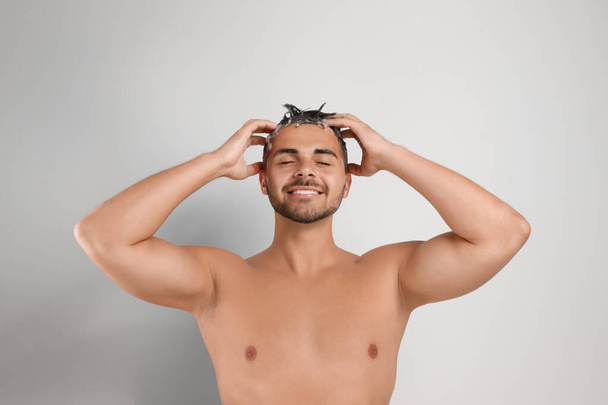 Young man washing hair on white background - Foto, afbeelding
