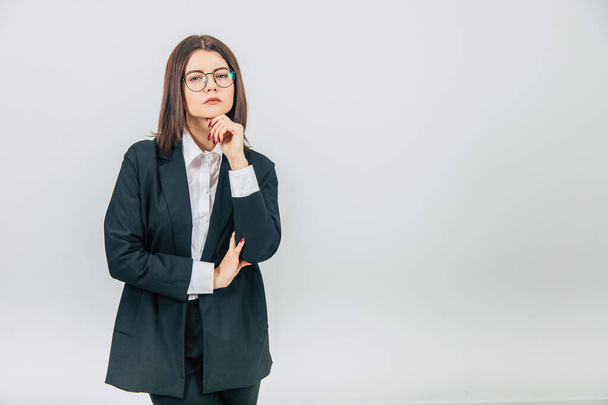 Attractive serious businesswoman in black suit standing, keeping hand on the chin, thinking, at the camera, narrowing her eyes. - Foto, afbeelding