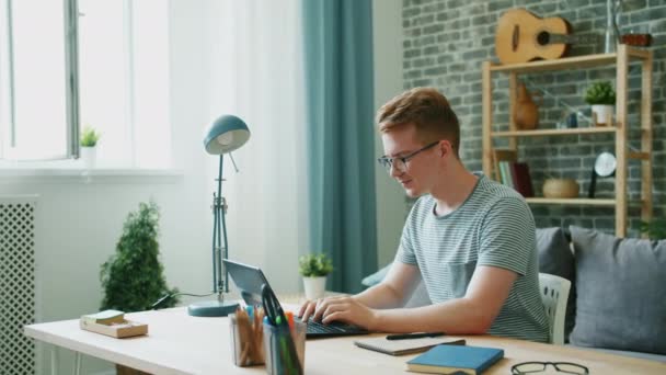 Happy teenager using laptop at desk at home typing enjoying communication - Filmati, video