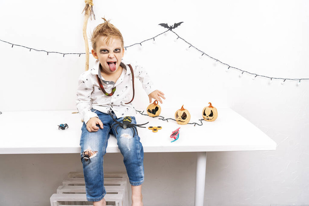 A little boy in a zombie costume sits on a table and makes grimaces. - Fotografie, Obrázek