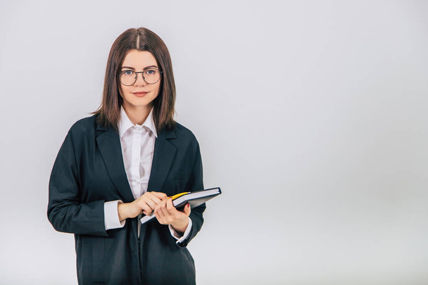 Young businesswoman in black suit holding a notebook and yellow pen, looking at the camera. - Fotografie, Obrázek