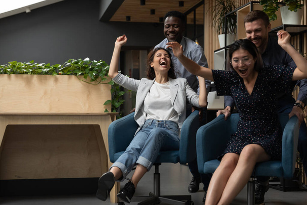 Four different ethnicity office workers having fun riding on chairs - Foto, Imagem