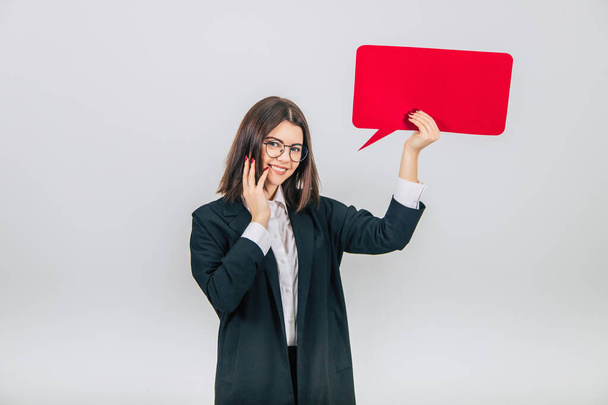 Portrait of an excited young business woman raising up empty square red speech bubble, looking at the camera, smiling lovely, keeping hand on her cheek. - Foto, Imagem