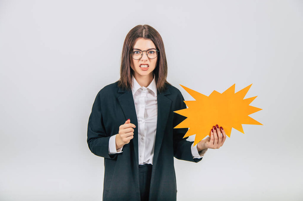 Excited young business woman holding an empty sparkle-like speech bubble, clenching her fists, setting her teeth, looking angry. - Foto, imagen