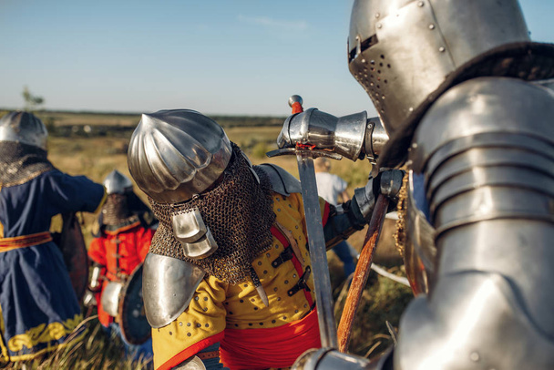 Medieval knights in armor and helmets fight with sword and axe. Armored ancient warrior in armour posing in the field - Photo, Image