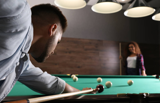 Young man playing billiard and blurred African-American woman on background. Space for text - Foto, immagini