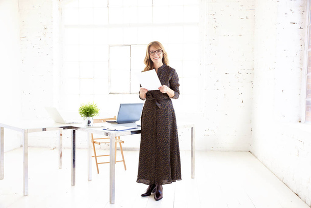 Full length shot of elegant businesswoman holding document in her hands while standing in the office and smiling to the camera. - Photo, image