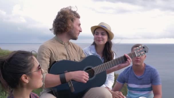 φλερτ, νεαρό χαρούμενο κορίτσι στην αγάπη φλερτάρει τα μάτια με τον άντρα που παίζει κιθάρα κατά τη διάρκεια πάρτι φίλων στη φύση - Πλάνα, βίντεο