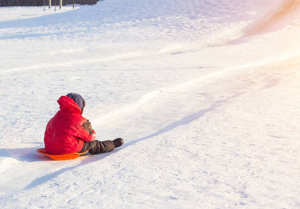 Little boy in bright red clothes rolls down a hill in frosty winter weather, copy space - Foto, Imagen