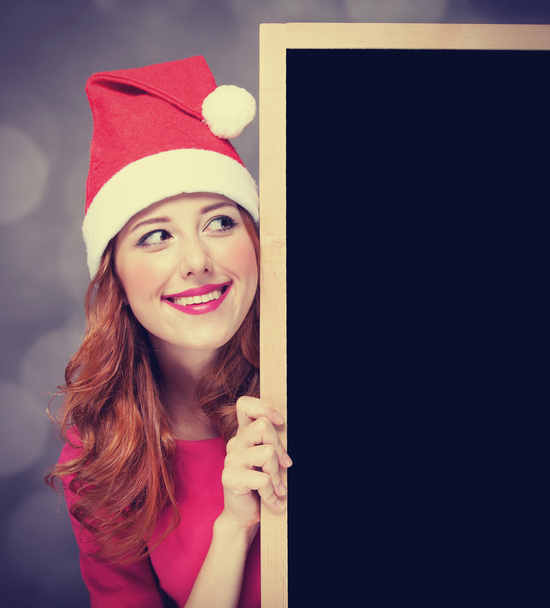 roodharige meisje in kerstmuts met blackboard - Foto, afbeelding