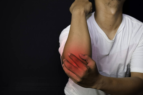 Homem asiático a segurar a mão. Ele sente dor no cotovelo com fundo preto. Conceito médico ou de saúde
 - Foto, Imagem