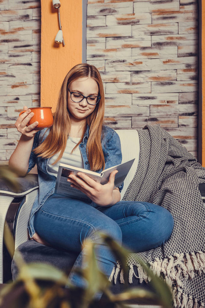 Šťastný dospívající dívka čtení knihy a pití čaje v křesle - Fotografie, Obrázek