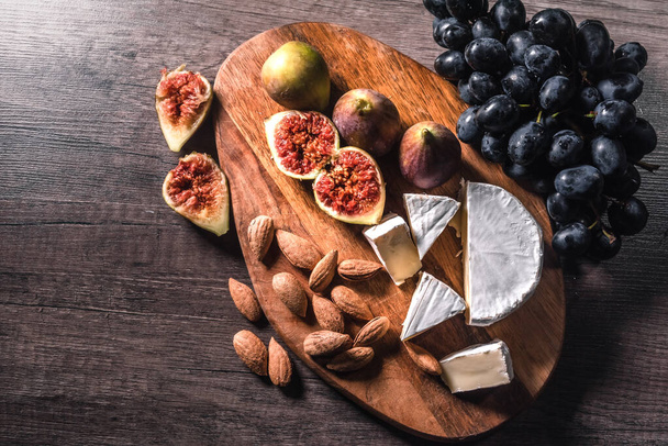 Cheese plate served with grapes, figs and nuts on a wooden background. - Zdjęcie, obraz