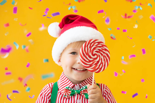 Happy child holding lollipop in hand against yellow background - Foto, imagen