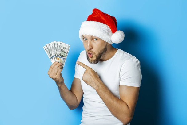 L'homme au chapeau de Père Noël tient de l'argent sur un fond bleu
.  - Photo, image
