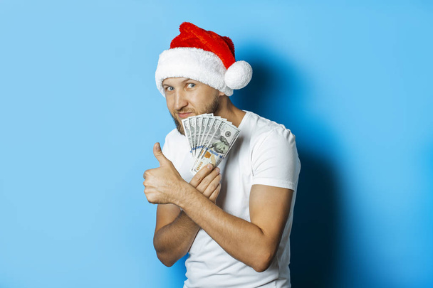 L'homme au chapeau de Père Noël tient de l'argent sur un fond bleu
.  - Photo, image