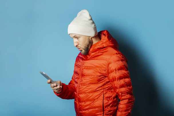 Man in a hat and a red jacket holds a mobile phone in his hands  - Foto, imagen