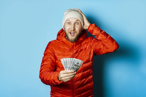 Man with a surprised face in a hat and a red jacket parka holds  - Photo, Image