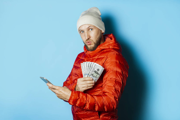Homem com um rosto surpreso em um chapéu e uma jaqueta vermelha mantém o dinheiro
  - Foto, Imagem