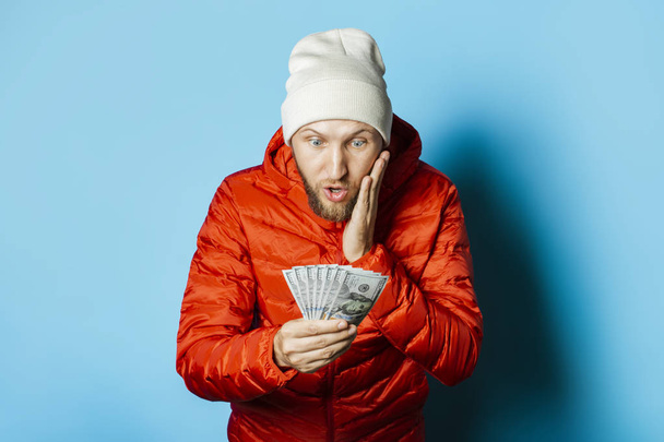 Man with a surprised face in a hat and a red jacket parka holds  - Photo, Image
