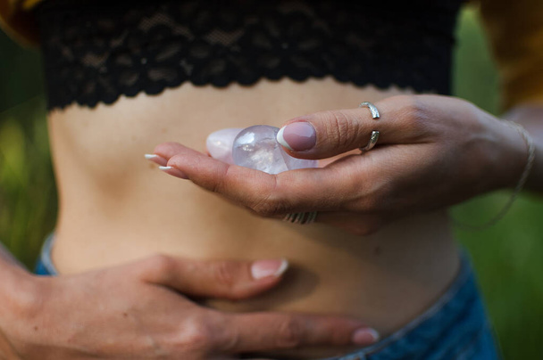 Female hands holding two yoni eggs for vumfit, imbuilding or meditation are made from pink quartz and transparent violet amethyst over her naked tummy outdoors - Photo, Image
